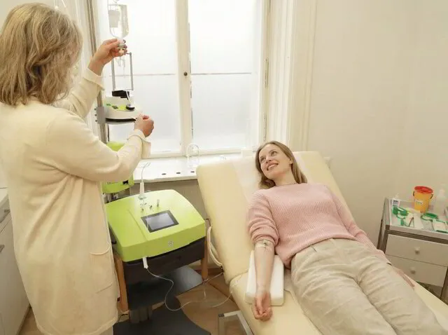 Ärztin bereitet eine Infusion für eine lächelnde Patientin auf der Behandlungsliege vor, neben modernem Ozontherapie-Gerät